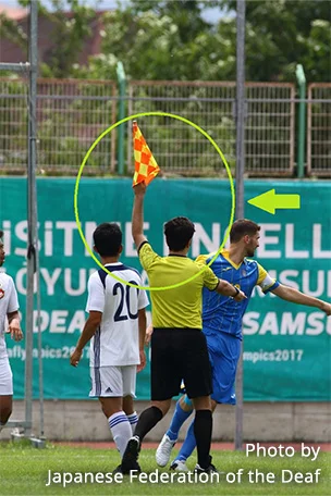 Photograph of a Referee signalling by waving a flag.